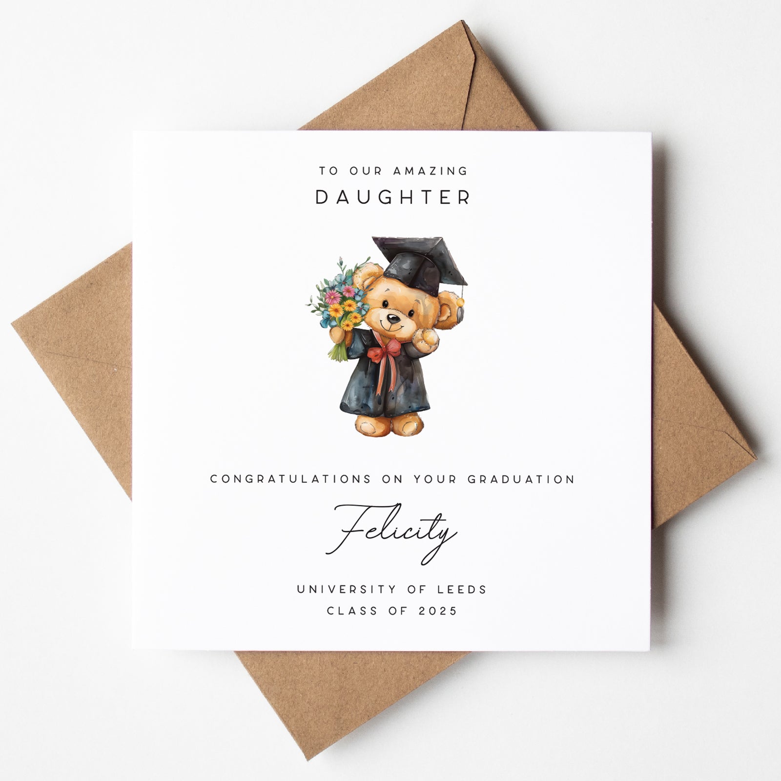 Personalised graduation card for a daughter, featuring a teddy bear in a graduation gown and cap holding a colourful bouquet. Text includes “To our amazing daughter,” the name “Felicity,” “University of Leeds,” and “Class of 2025.” Card is shown with a kraft brown envelope.