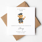 Personalised graduation card for a son, featuring a teddy bear in a cap and gown holding a diploma scroll. Text reads “To our amazing son” with the name “Harry,” “University of Bath,” and “Class of 2025.” Card is paired with a kraft brown envelope.