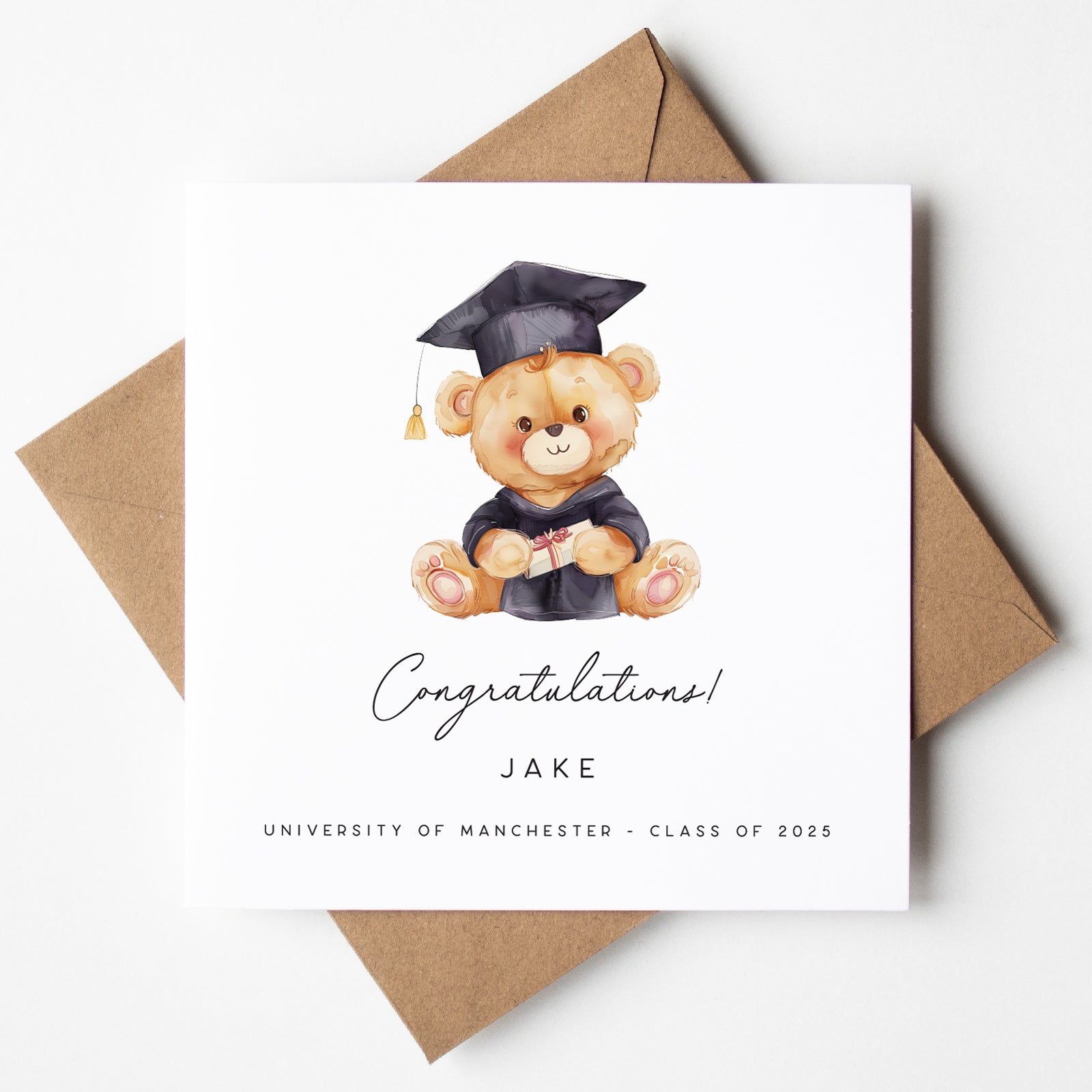 Personalised graduation card featuring a teddy bear in a black cap and gown holding a wrapped diploma. Custom text includes “Congratulations,” the name “Jake,” and “University of Manchester – Class of 2025.” Card is displayed with a kraft brown envelope.