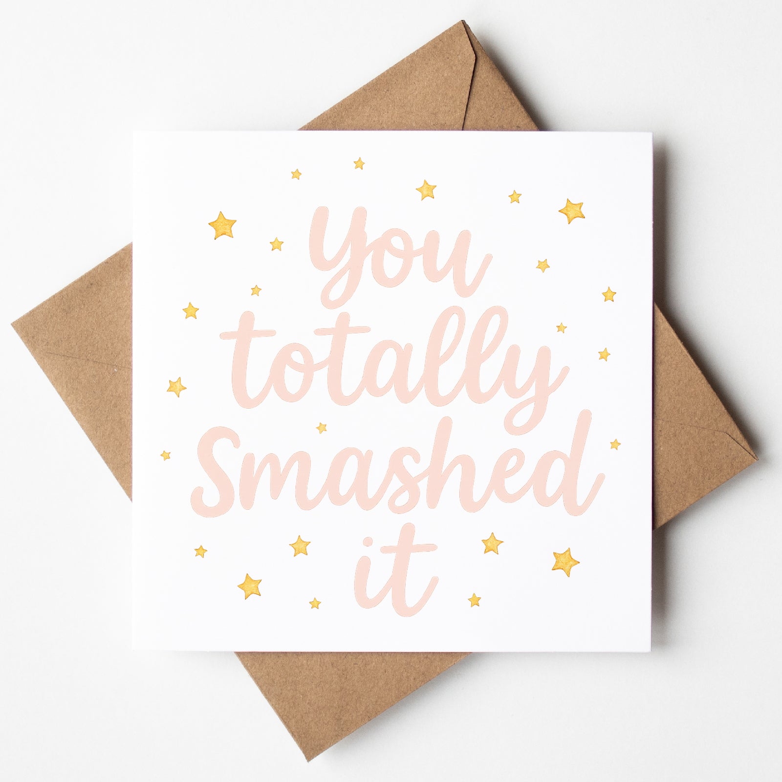 Pink and gold star-themed graduation card with the message “You totally smashed it” in soft script font. Displayed with a kraft brown envelope.